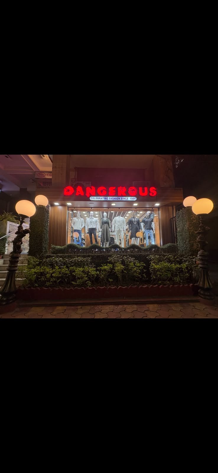 Dangerous Fashion frontage at night framed by hedges and lamp posts